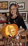 Kvinne holder en utskåret gresskarlykt med portrett foran kunstverk.