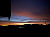 Fargerik solnedgang over et mørkt landskap i silhuett.