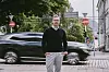 Mann på fortauet foran en passerende svart SUV i en bygate.