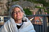 Kvinne med briller og lys jakke foran en steinmur og et svart rekkverk.