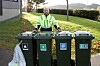 Renovasjonsarbeider i refleksjakke bak fire avfallsbeholdere ved et boligområde.