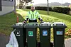 Renovasjonsarbeider i refleksjakke bak fire avfallsbeholdere ved et boligområde.