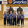 Barn og voksne i blå håndballdrakter poserer sammen i en idrettshall.