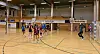 Håndballspillere i aksjon på en innendørsbane med mål og tribuner.