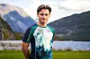 Mann i grønn og hvit sportsdrakt foran en fjord omgitt av fjell.