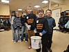 Barn står samlet i et skolelokale; to gutter foran holder en innsamlingsbøtte.