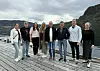 Åtte personer poserer på en trebrygge med fjord og fjell i bakgrunnen.