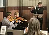Fløytist og to fiolinister spiller kammermusikk foran et publikum.