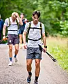 Sportsutøver går på en grussti med gåstaver, fulgt av andre deltakere i skogen.
