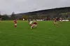 Fotballspillere i rødt og hvitt kjemper om ballen på en grønn gressbane.