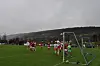 Fotballspillere foran målet på en våt bane under en overskyet himmel.