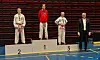 Tre kampsportutøvere på seierspallen sammen med en funksjonær i en idrettshall.