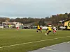 Fotballspillere i gule og hvite drakter kjemper om ballen på en grønn bane.