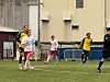 Fotballspillere i hvite og gule drakter spiller på en kunstgressbane.