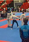 Dommer mellom to taekwondoutøvere på en blå og rød konkurranseflate.