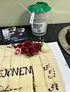 Dekorert kremkake med røde roser, hvit blomst, kopp og smarttelefon på en kjøkkenbenk.