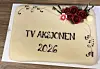 Lys kake med teksten «TV AKSJONEN 2026» og rosedekor på et trebord.