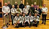 Blåseorkester poserer med flere messinginstrumenter i en trepanelert sal.
