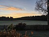 Frostlagt åkerlandskap ved solnedgang, med skog, gjerde og busker i forgrunnen.