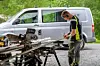 Arbeider i verneutstyr ved metallutstyr foran en hvit varebil.