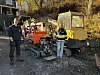 To personer ved anleggsmaskiner, blant annet en gul beltegraver, på et gruslagt område.