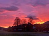 Hus i silhuett foran en rosa og oransje solnedgang.