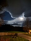 Dramatiske skyer over skog og eng, med lys gjennom skydekket og en opplyst grusvei.