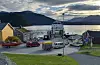 Ferje ved kai i en liten kystby med fjord, fjell og bolighus i bakgrunnen. Utrykningsbiler fra brannvesenet og politibiler på ferjekaia.