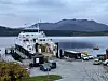 Bilferge ved kai med kjøretøy, fjord og fjell i bakgrunnen.