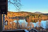 Innsjø med høstskog og fjell sett fra en terrasse under blå himmel.