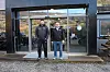 To personer står foran en glassinngang til en moderne bygning.