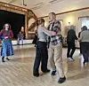 Et par danser på et samfunnshus mens andre deltakere danser i bakgrunnen.