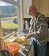 Mann lager mat ved kjøkkenbenken med grønnsaker og ingredienser foran et vindu.