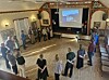 Mennesker står i ring for å danse i en historisk sal.