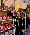 Butikkmedarbeider holder opp en rød sesongvare foran hyller med julepynt.