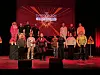 Teatergruppe samlet på en rødt opplyst scene foran en grafisk bakgrunn.