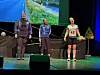 Tre damer står på en scene med treningsklær, ei av de med startnummer.