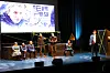 Syv mennesker på scenen med bilde av et ansikt i bakgrunnen på et lerret.
