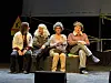 Fire skuespillere sitter på en benk på en opplyst teaterscene.