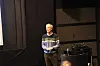 Mann på en mørklagt scene foran scenetepper og teknisk utstyr.