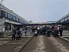 Folkemengde ved en bygning på en våt, brosteinslagt plass.