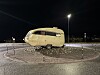 Kremfarget, eldre campingvogn står midt i en rundkjøring om natten.