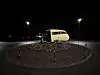 Kremfarget, eldre campingvogn står midt i en rundkjøring om natten.
