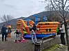 Mennesker ved en oransje oppblåsbar lekeinstallasjon på et torg med fjell i bakgrunnen.